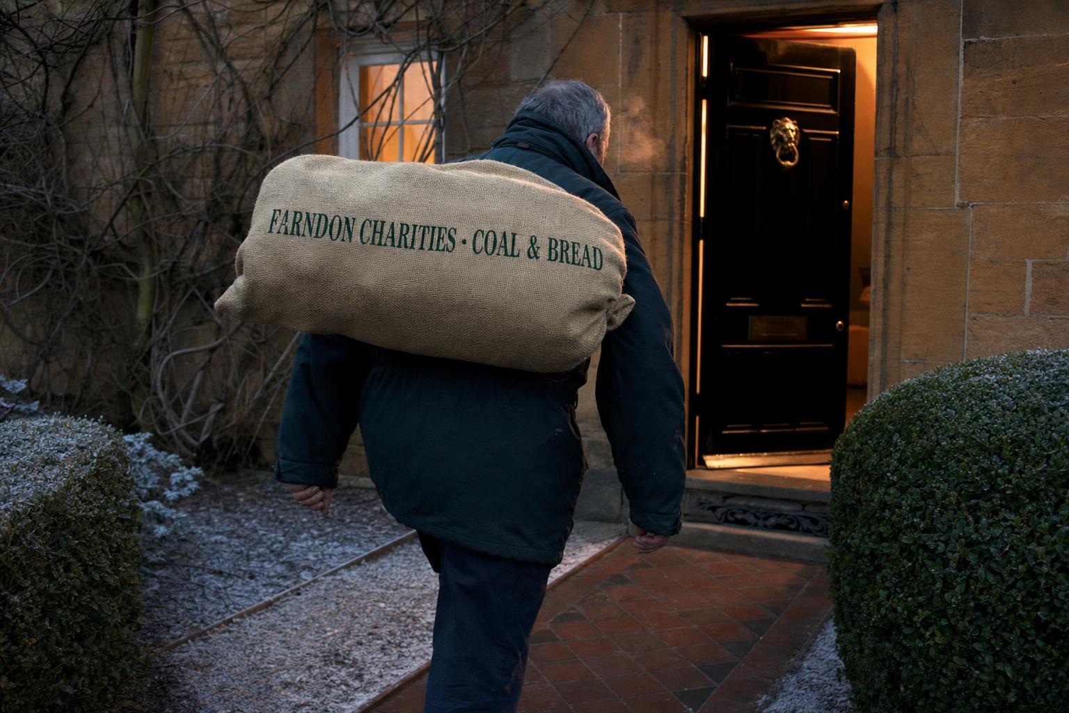A volunteer carrying a hessian bag of coal to a Farndon doorstep at dusk in December